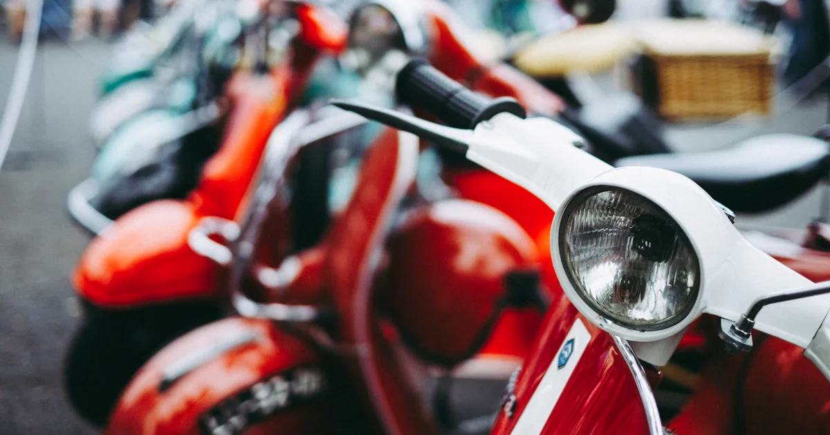 Fileira de motos de entrega vermelhas estacionadas na rua, capa do guia de entregadores e rotas no delivery