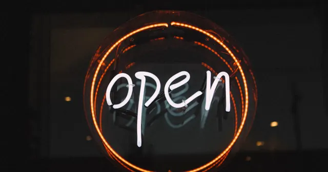 Letreiro de neon redondo aceso na fachada escura de uma loja aberta, capa do guia de horário de funcionamento do delivery