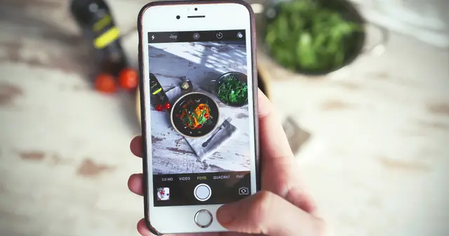 Mão segurando um celular que fotografa um prato montado, capa do guia de link de cardápio para Instagram e WhatsApp